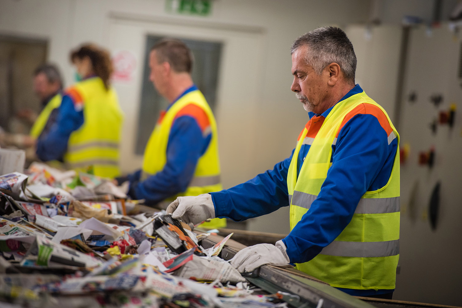 Workers sorting papers on factory assembly line for recycling at recycling plant.